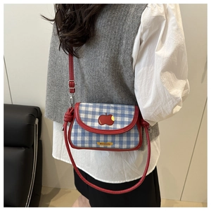 Détail du sac bandoulière à carreaux bleus avec bordure en cuir rouge et pomme brodée