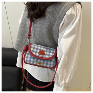 Détail du sac bandoulière à carreaux bleus avec patch pomme rouge et finitions en cuir
