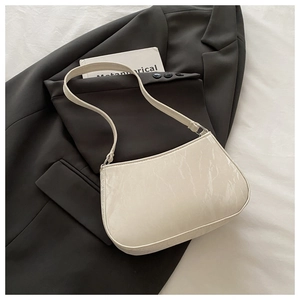 Détail d'un sac demi-lune crème avec texture marbrée posé sur une veste de costume
