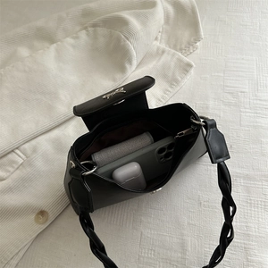 Minimalist black underarm bag with woven handle and silver bow lock on white background