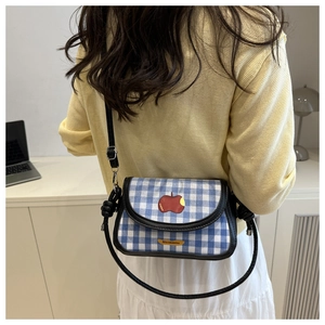 Détail du sac bandoulière à carreaux bleus avec patch pomme rouge et bandoulière