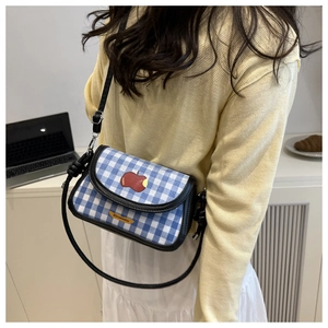 Détail du sac à carreaux bleu et blanc avec broderie pomme rouge et bandoulière en cuir