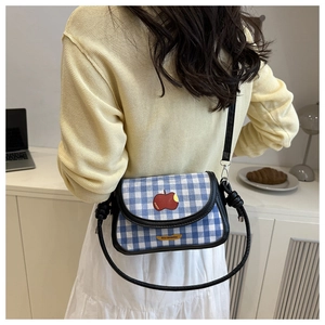 Sac bandoulière à carreaux bleus et blancs avec écusson pomme rouge porté par un mannequin