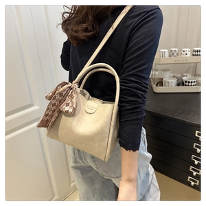 Detail of beige leather bucket bag featuring decorative silk scarf and handle branding