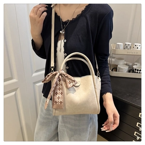 Detail of a beige handbag with a brown plaid scarf accent on the handle shown in use