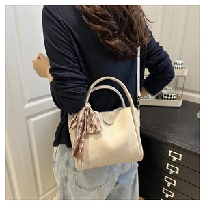 Beige bucket bag with plaid silk scarf and long shoulder strap worn by a model