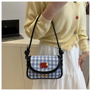 Détail d'un sac à carreaux bleus et blancs avec écusson pomme rouge et nœud sur la bandoulière