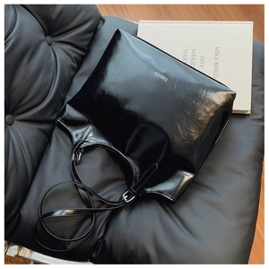 Detail of glossy black tote bag with white fashion text on a black leather surface