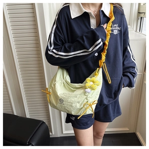 Detail of light green pleated crossbody bag with yellow strap and flower charm on model