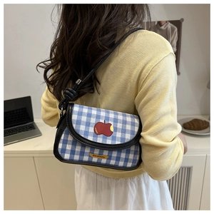 Détail du sac de selle à carreaux bleus avec broderie pomme rouge et bandoulière noire