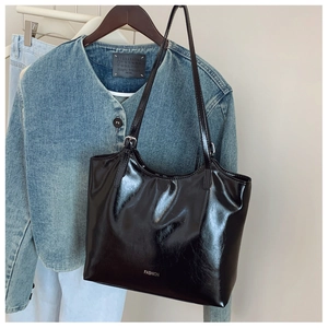 Detail shot of black glossy leather tote bag with FASHION logo and smooth texture