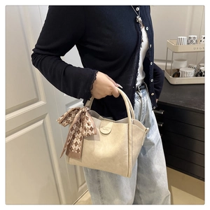 Close-up of beige leather bucket bag with a stylish checkered silk scarf on the handle