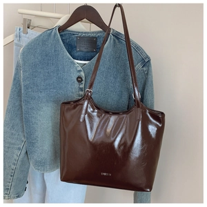 Close-up of glossy brown tote bag with silver FASHION text hanging on wooden hanger