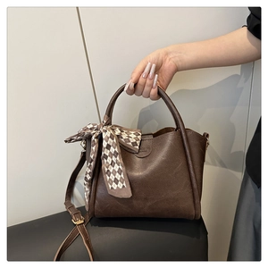 Detail of a brown retro bucket bag with a checkered silk scarf handle and embossed text
