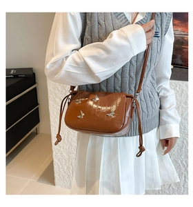 Detail of caramel glossy crossbody bag featuring silver butterfly buckles and drawstring