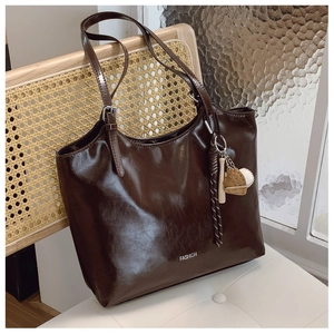 Detail of dark brown tote bag with baseball charms on a white tufted bench background