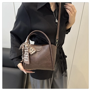 Detail of dark brown leather bucket bag with silk scarf handle on model's shoulder