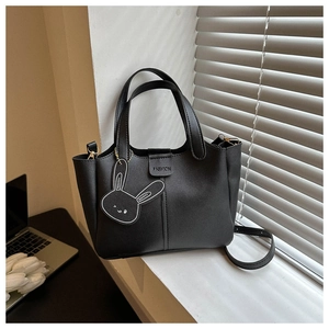 Close-up of black bucket bag featuring a fashion bunny pendant on a windowsill