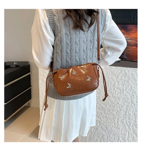 Close-up of brown patent leather bucket bag with metallic butterfly details and shoulder strap