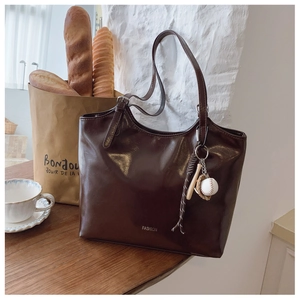 Detail of dark brown leather tote bag with baseball charm in an elegant lifestyle setting