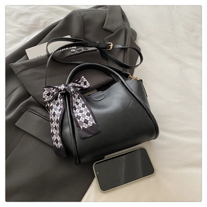 Detail of black matte leather bucket bag with decorative plaid scarf on a grey blazer