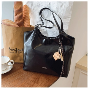 Close-up of black glossy tote bag with FASHION text and a baseball charm on wood desk