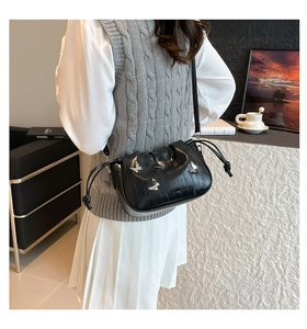 Detail of black PU leather bucket bag with silver butterfly emblem and drawstring