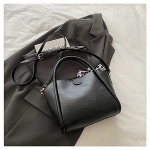 Detail of a black matte bucket bag with a silk scarf accent on a stylish blazer