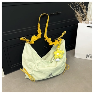 Detail of light green pleated nylon crescent bag with yellow ruffled strap and floral charm