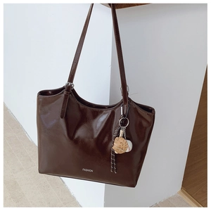 Detail of dark brown glossy leather tote bag with silver buckle and fashion pendant