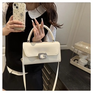Detail view of cream handbag featuring shiny finish and silver rhinestone G buckle decor