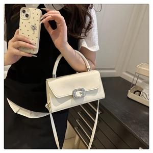 Detail of white square handbag showing luxury rhinestone G buckle and shiny leather texture