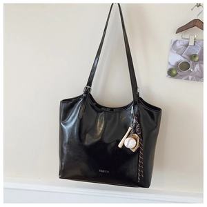 Detail of black glossy patent leather tote bag with FASHION logo and baseball charms