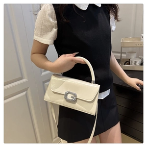Detail of elegant cream patent leather handbag with silver G buckle and thin strap