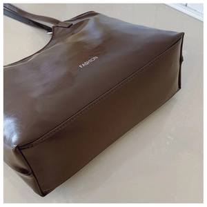 Detailed side view of dark brown high-shine leather tote bag with FASHION lettering