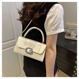 Close-up of white patent leather shoulder bag with sparkling silver G-buckle detail