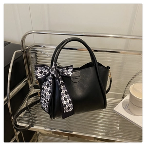 Close-up of black leather bucket bag with checkered scarf and engraved logo detail