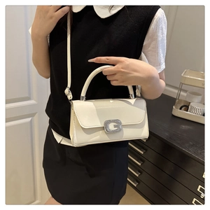 Detail of white leather crossbody bag with silver G-buckle on a dark wooden background