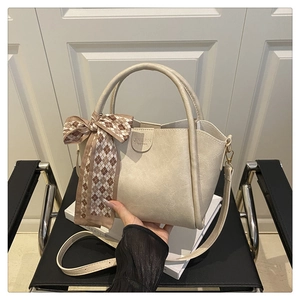 Detail of minimalist cream bucket bag featuring a silk scarf handle and leather texture