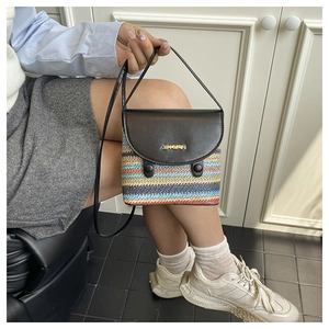 Detail view of a colorful woven crossbody bag with brown leather flap and gold metal logo