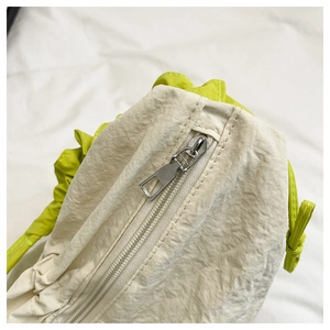 Detail shot of off-white textured fabric bag with bright neon green handles and silver zipper