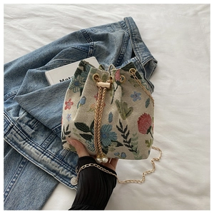 Détail de broderie florale sur sac seau en toile avec chaîne dorée et perle décorative