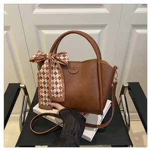 Close-up of brown textured leather bucket bag with vintage plaid scarf and brand logo