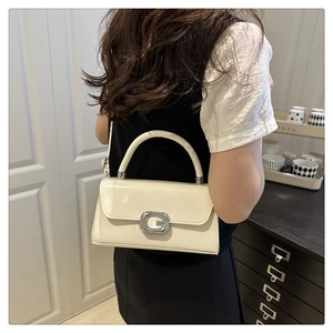 Detail of a chic cream leather handbag featuring a large metallic G buckle and strap