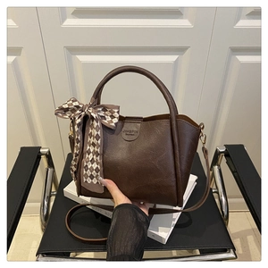 Detailed macro view of dark brown litchi grain leather bucket bag with silk scarf detail