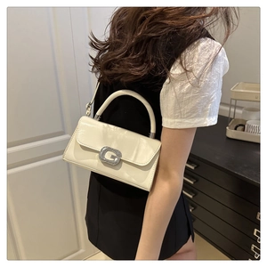 Detail einer weißen glänzenden Handtasche mit auffälliger G-Schnalle aus Silber