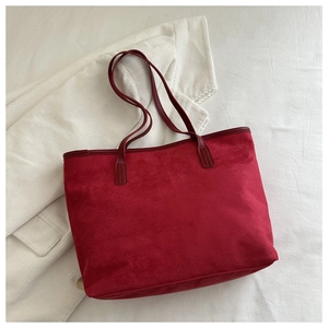 Detail shot of a large red suede tote bag showing soft texture and reinforced stitching