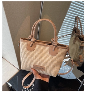 Detail of woven straw tote bag with brown leather handles and adjustable shoulder strap