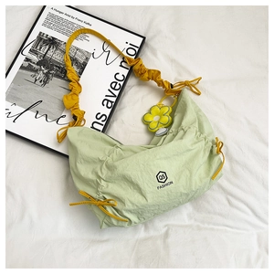 Detail of light green pleated crossbody bag with yellow strap and flower charm