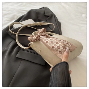 Detail of off-white bucket bag featuring a decorative brown silk scarf handle wrap